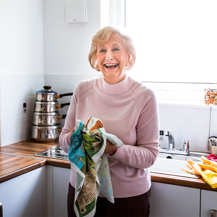 Smiling elderly woman holding kitchen towel in hands