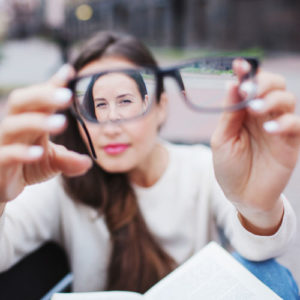 a woman holds up a pair of glasses to the camera lens to show focal difference
