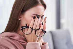 Portrait view of tired young woman feeling pain eyestrain and rubbing dry irritated eyes while sitting at the sofa after hardworking with her laptop. Stock photo