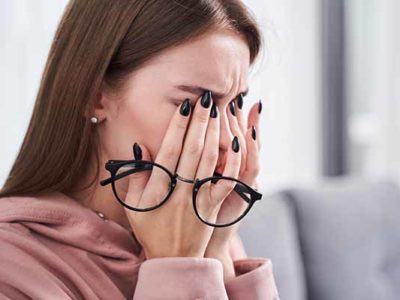 Portrait view of tired young woman feeling pain eyestrain and rubbing dry irritated eyes while sitting at the sofa after hardworking with her laptop. Stock photo