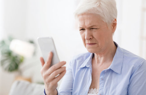 Myopia Concept. Elderly woman squinting while looking at smartphone screen